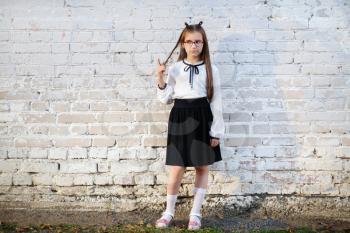 Schoolgirl standing against white brick wall background. Child girl in school uniform posing.