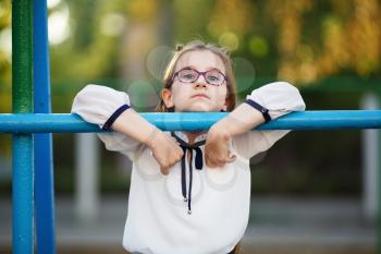 Pensive child girl leaning on the horizontal bar. Schoolgirl with glasses looking at the camera. Selective focus.