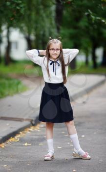 Schoolgirl in a school uniform posing. Child girl stands outdoors. Vertical shot. Selective focus.