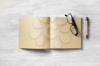 Opened book with blank craft paper pages, pen and glasses on light wooden background. Flat lay.