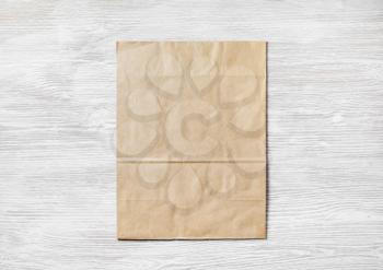 Crumpled kraft paper bag on light wooden background. Blank recyclable package. Top view. Flat lay.