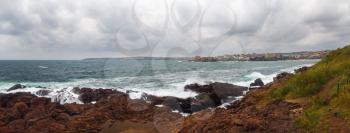Waves crashing on rough shores. Sea waves crash and splash on rocks. Panoramic shot.