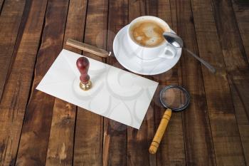 Vintage postal stationery. Blank envelope, magnifier, coffee cup, stamp and spoon on wooden background. Responsive design mock up.
