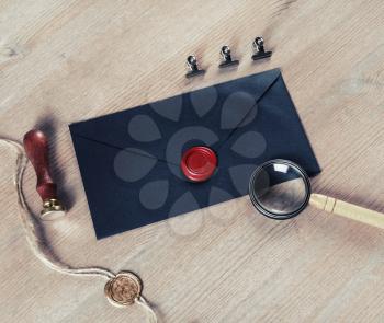 Old black envelope with red wax seal, magnifier and stamp on wooden background.