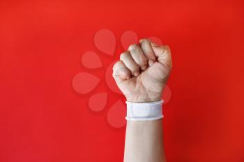 Clenched fist female hand with white bracelet on red backgroung.