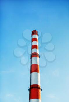 Factory chimney against blue sky background. Vertical shot.