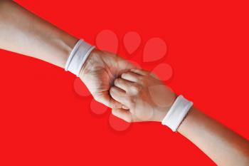 Helping hand to a friend. Female hands with white bracelets on red backgroung.