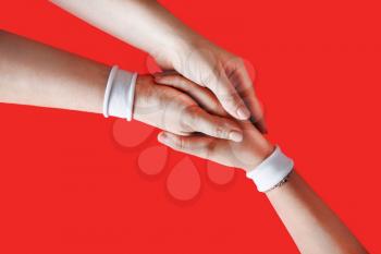 Hands with white bracelets unite with eachother as friends greeting on red backgroung.
