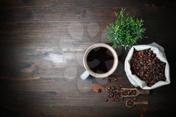 Delicious fresh coffee. Coffee cup, coffee beans in canvas sack and plant on vintage wood table background. Flat lay.