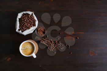 Still life with coffee cup, coffee beans in canvas bag and ground powder on wooden background. Copy space for your text. Flat lay.