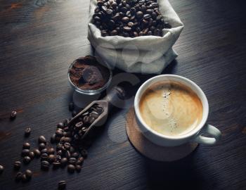 Cup of tasty coffee, coffee beans and ground powder on vintage wooden background.