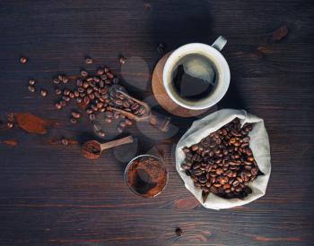 Photo of fresh tasty coffee on vintage wood table background. Coffee cup, coffee beans in canvas bag and ground powder. Top view. Flat lay.