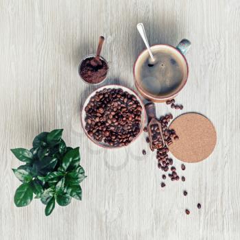Still life with coffee cup, coffee beans, plant, ground powder and beer coaster on light wood table background. Top view. Flat lay.