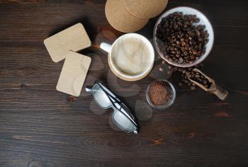 Coffee cup, kraft business cards, roasted coffee beans, glasses and coffee ground on wood table background. Flat lay.