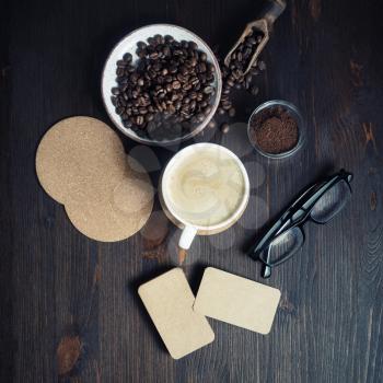 Composition with coffee cup, kraft business cards, coffee beans, glasses and ground powder on vintage wood kitchen table background. Flat lay.