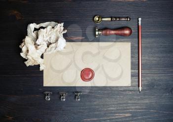Blank kraft paper envelope with wax seal, stamp, spoon, pencil and crumpled paper on vintage wooden background. Retro postal stationery. Flat lay.