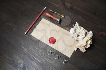 Blank kraft paper envelope with red wax seal, stamp, spoon, pencil and crumpled paper on wooden background. Mockup for your design.