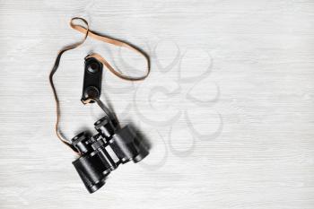 Photo of vintage black binoculars on light wood table background. Copy space for your text. Flat lay.
