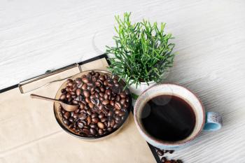Still life with coffee cup, plant and coffee beans on light wood table background.