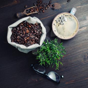 Vintage still life with coffee cup, roasted coffee beans, plant and glasses on wooden background. Flat lay.