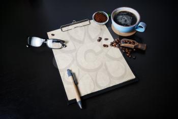 Menu and coffee. Clipboard with blank kraft letterhead, pen, coffee cup, coffee beans, pen, glasses and ground powder on black table background.