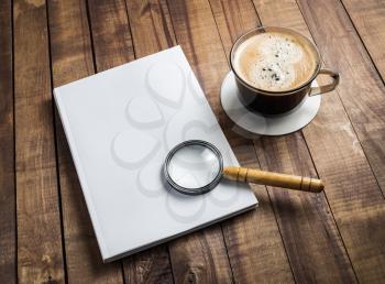 Blank book, magnifier and coffee cup on wooden background.