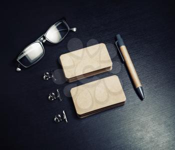 Blank kraft business cards, pen and glasses on black wooden background. Template for branding identity.