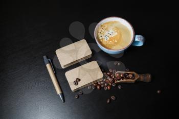Blank kraft business cards, coffee cup, roasted coffee beans and pen on black wooden background.