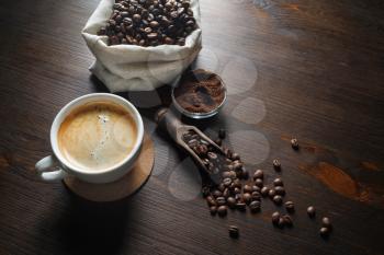 Coffee cup, coffee beans and ground powder on wooden kitchen table background.