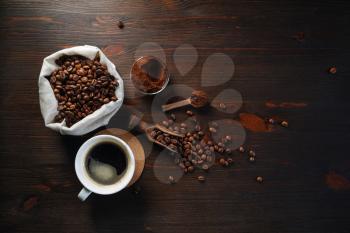 Still life with coffee. Cup of coffee, roasted coffee beans in a sack and ground powder on wooden kitchen table background. Flat lay.