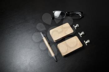 Blank kraft stationery set on black wooden background. Business cards, pen and glasses. Template for branding identity.
