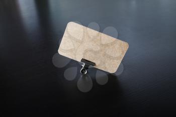 Photo of blank kraft business card in metal binder clip on black wooden background.