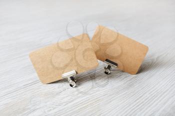 Two blank kraft business cards and metal binder clips on light wood table background.