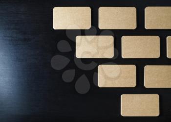 Many blank kraft business cards on black wooden background. Flat lay.