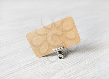 Blank kraft business card in metal binder clip on light wooden background.