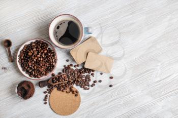 Photo of fresh tasty coffee on light wood kitchen table. Coffee cup, coffee beans, ground powder, beer coaster and blank kraft business cards. .Flat lay.