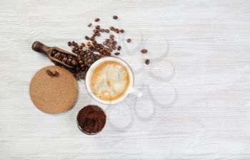Coffee cup, roasted coffee beans, coffee ground and beer coaster on light wood table background. Top view with copy space for your text. Flat lay.