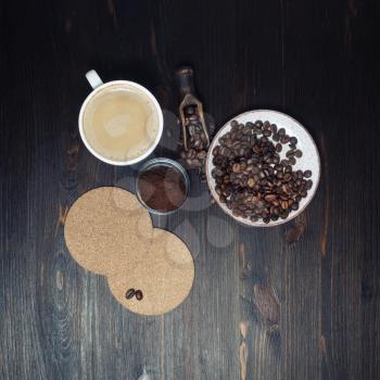 Fresh delicious coffee with milk cup, roasted coffee beans, beer coasters and ground powder on wood kitchen table background. Top view. Flat lay.