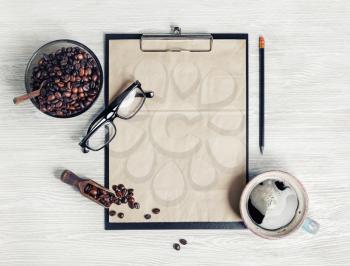 Menu and coffee. Clipboard with blank kraft letterhead, coffee cup, coffee beans, glasses and pencil on light wooden background. Top view. Flat lay.