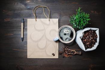 Blank kraft paper bag, coffee cup, plant, coffee beans in canvas bag and pen on wooden background. Top view. Flat lay.