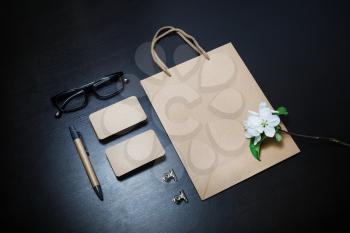 Stationery set. Kraft paper bag, business cards, pen, glasses and flowers on black table background.
