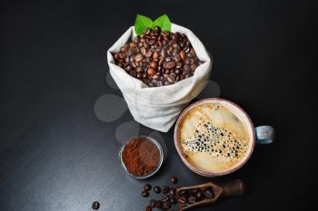 Coffee cup, coffee beans and ground powder over black kitchen table background.