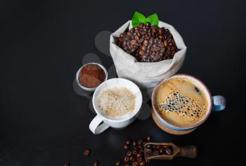 Fresh delicious coffee. Coffee cups and coffee beans in canvas bag and ground powder on black wooden background.