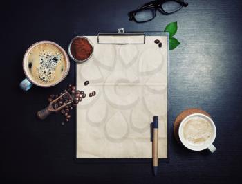 Clipboard with blank kraft letterhead, coffee cups, roasted coffee beans, pen and coffee ground on black table background. Space for text. Top view. Flat lay.