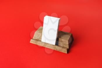 Wooden holder with blank business cards on red paper background.