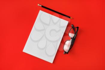 Blank copybook, pencil and glasses on red paper background. Template for branding identity. Top view. Flat lay.