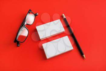 Photo of blank stationery set. Business cards, glasses and pencil on red paper background. Template for placing your design.