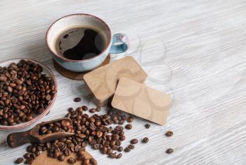 Blank kraft paper business cards, coffee cup and coffee beans on light wooden background.