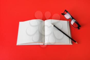 Photo of blank book, pencil and glasses on red paper background. Responsive design mockup. Stationery elements. Template for placing your design.