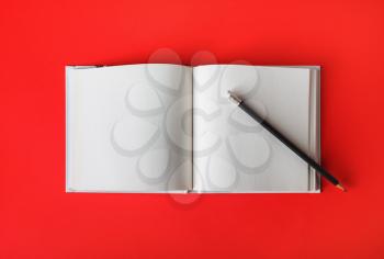 Photo of open book with blank pages and pencil on red paper background. Responsive design template. Flat lay.